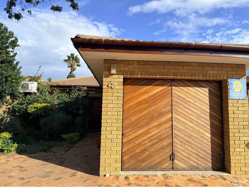 Front elevation of the property featuring a brick facade, timber garage doors, and a paved driveway entrance.