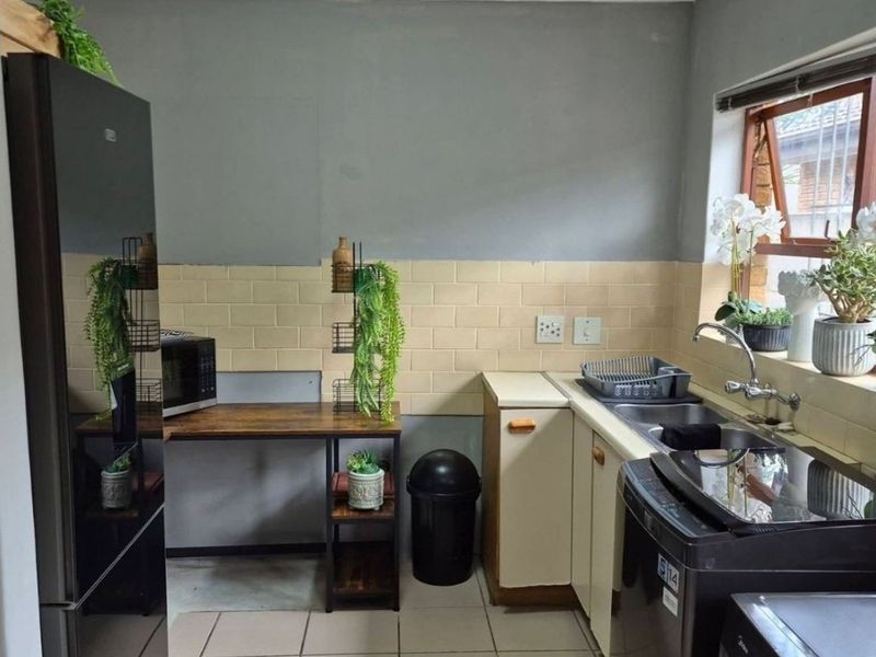 A functional scullery area featuring a double basin sink, tiled splashback, and built-in cabinetry with a window providing natural light.