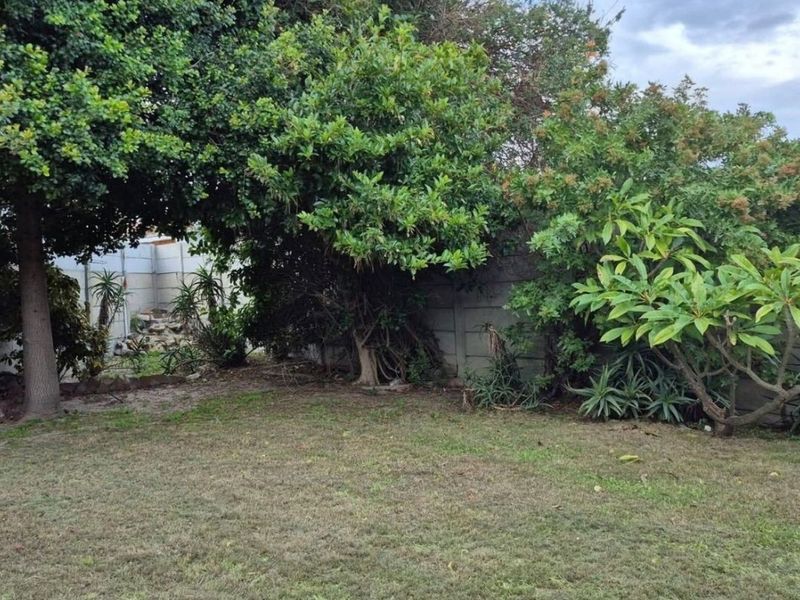 A private rear garden featuring a lawn area, mature trees, and a precast concrete boundary wall.