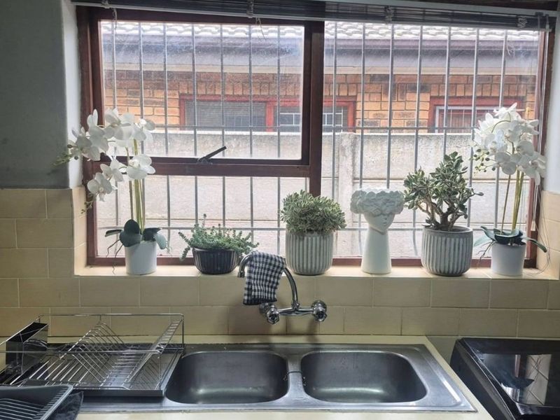 Kitchen sink area featuring a double bowl stainless steel sink, chrome mixer tap, and tiled splashback set against a window with security bars.