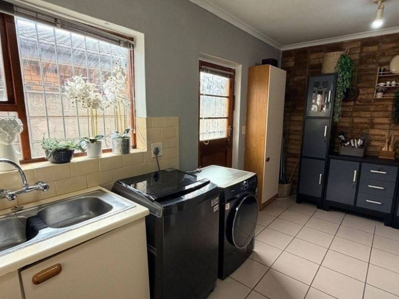 Functional laundry room featuring a stainless steel sink, tiled splashback, tiled flooring, and a distinctive brick feature wall with direct exterior access.