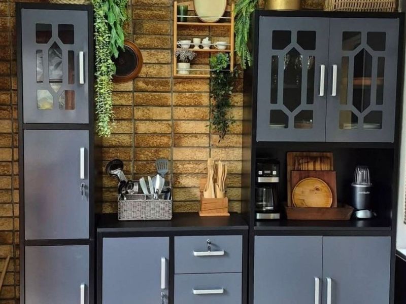 A kitchen area featuring dark grey built-in cabinetry set against a textured brick feature wall with window blinds.
