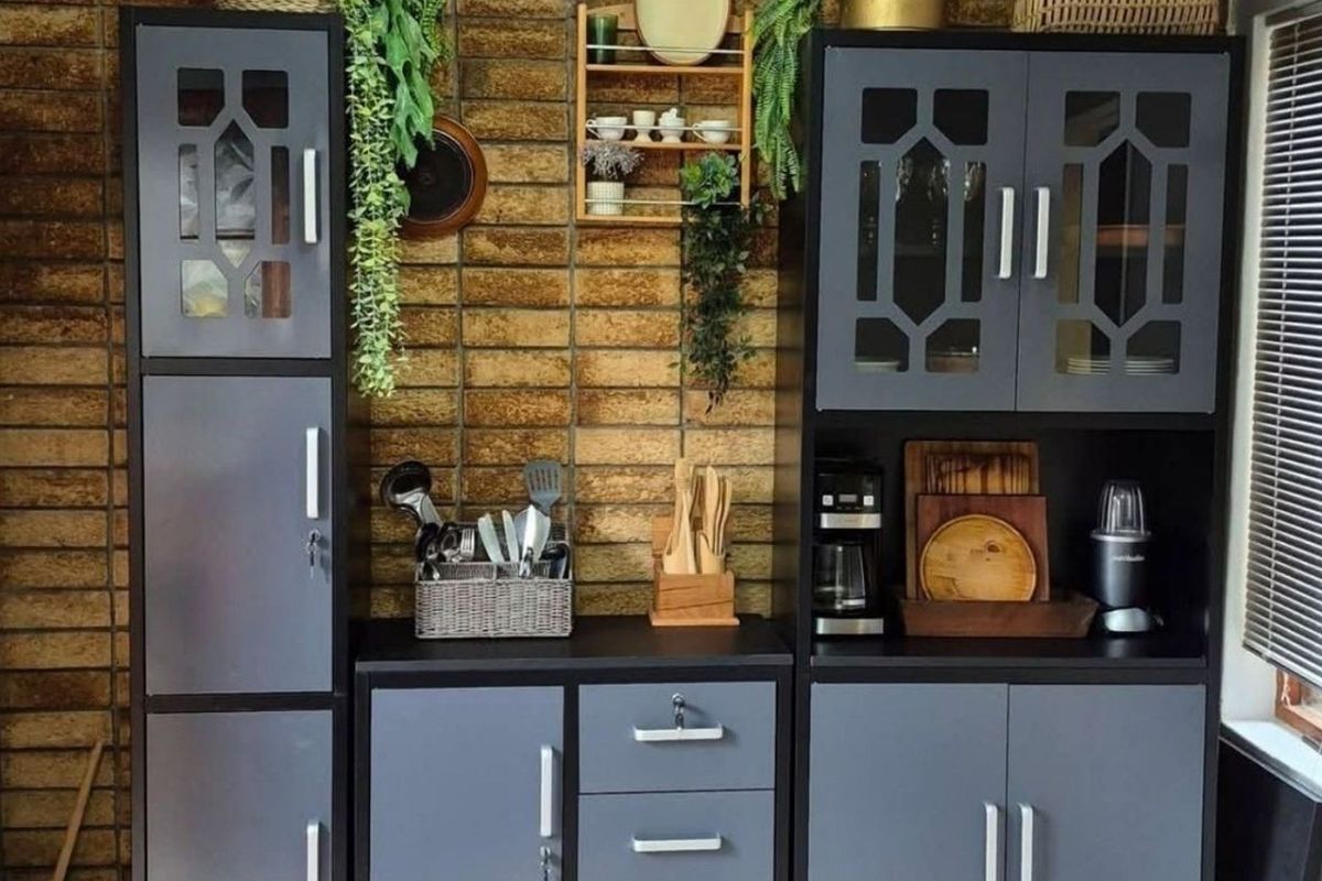 A kitchen area featuring dark grey built-in cabinetry set against a textured brick feature wall with window blinds.
