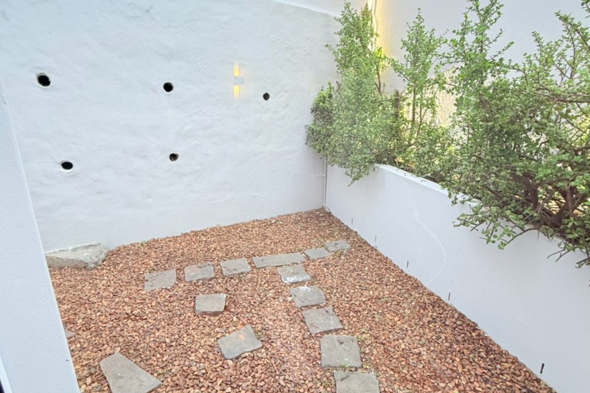 A private courtyard area featuring a gravel ground cover, stone stepping path, and a raised planter bed against a white boundary wall.