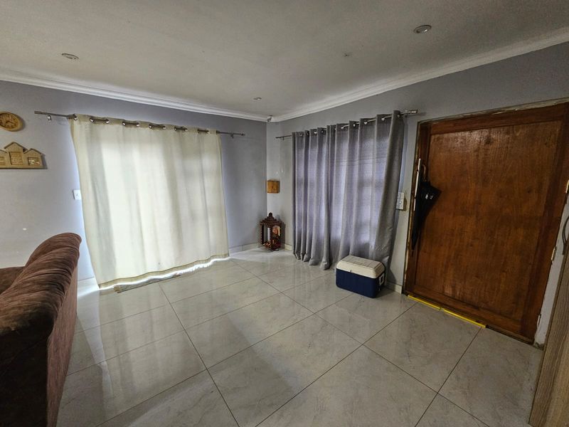 A living area featuring large format floor tiles, recessed downlighting, and a solid wood entrance door with neutral wall finishes.