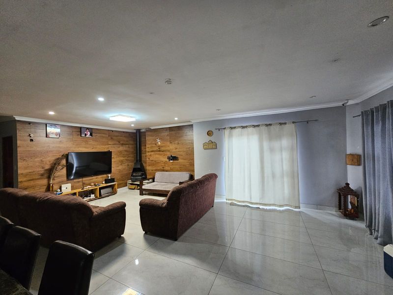 Spacious living room featuring wood-look accent wall paneling, a freestanding fireplace, large format floor tiles, and direct access to the outdoors via sliding doors.