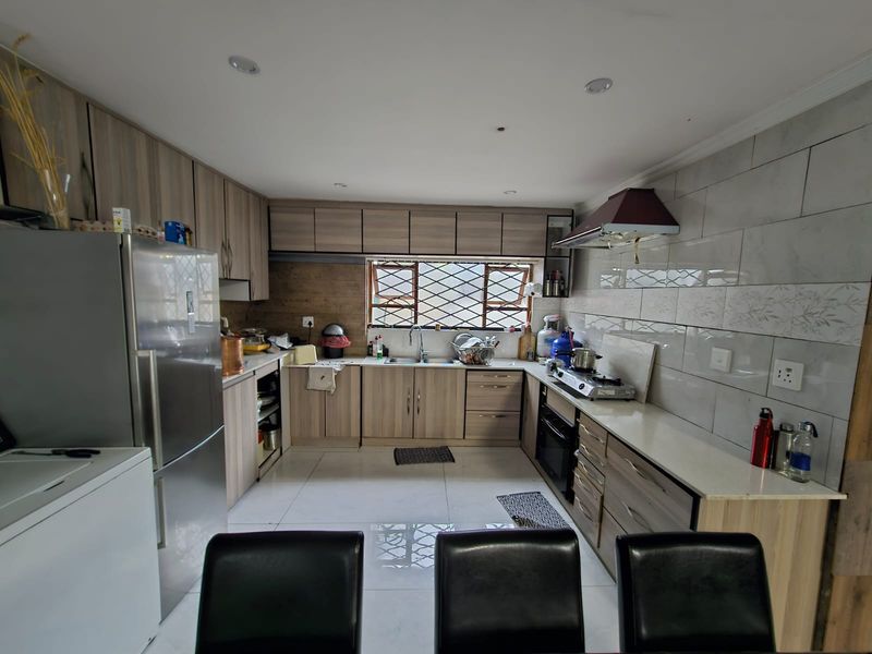 A functional kitchen featuring modern wood-look cabinetry, stone countertops, a built-in oven, extractor fan, and tiled backsplash with security bars on the window.