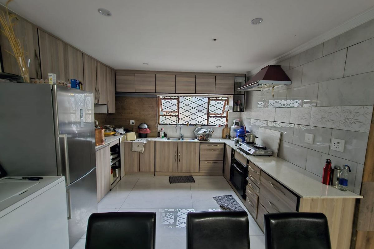 A functional kitchen featuring modern wood-look cabinetry, stone countertops, a built-in oven, extractor fan, and tiled backsplash with security bars on the window.