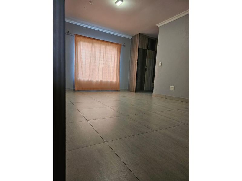 A spacious, empty bedroom featuring neutral tiled flooring, built-in cupboards, and coving detail, offering a clean canvas for personalization.