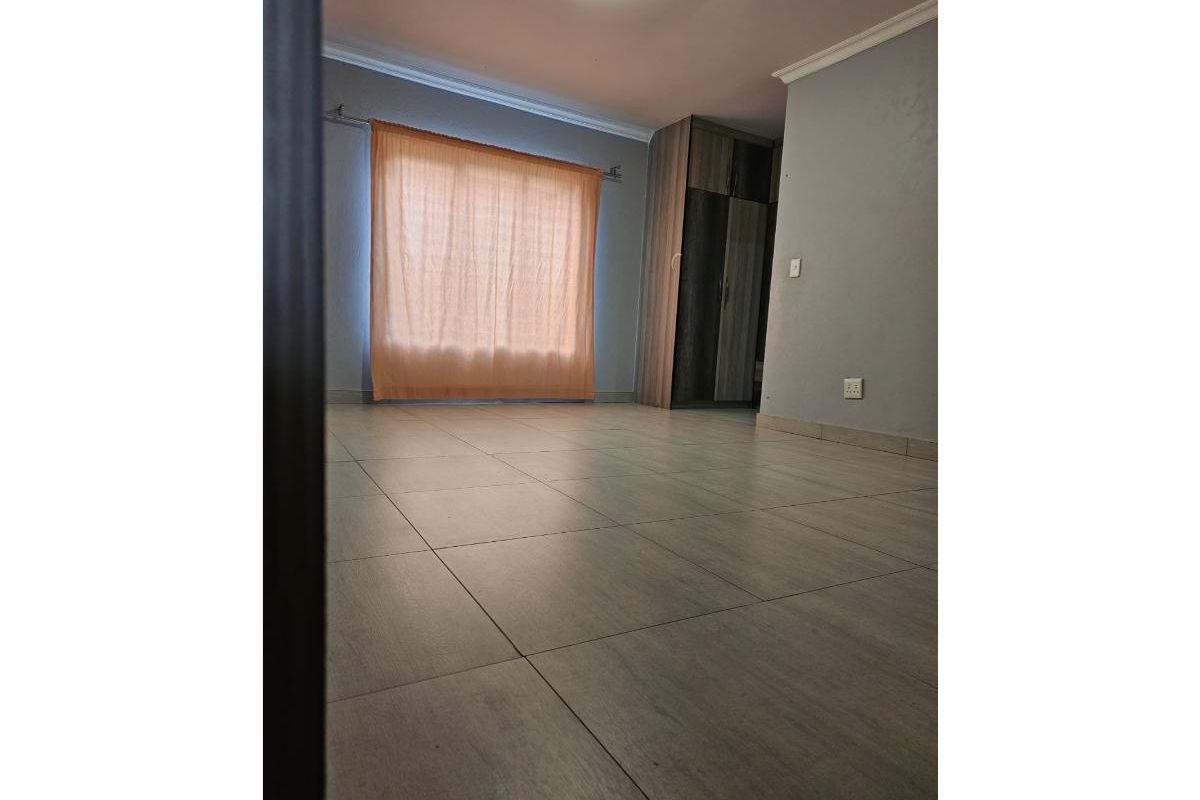 A spacious, empty bedroom featuring neutral tiled flooring, built-in cupboards, and coving detail, offering a clean canvas for personalization.