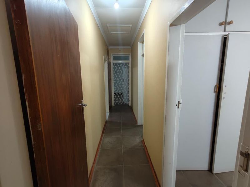 A functional hallway featuring tiled flooring, built-in storage cupboards, and a security gate at the end, providing access to various rooms.