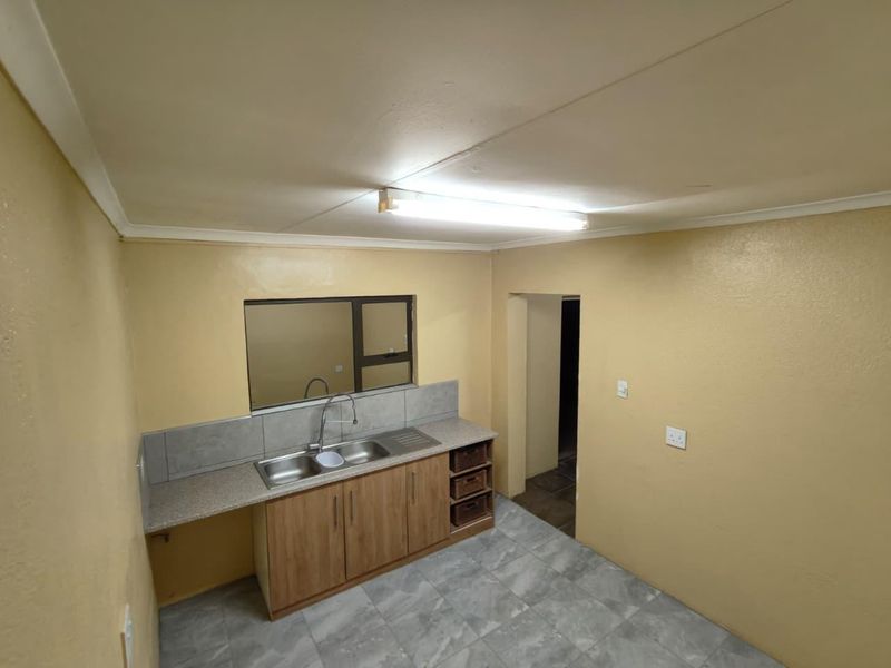 A functional kitchen area featuring wood-finish cabinetry, a stainless steel double sink, tiled backsplash, and neutral tiled flooring.