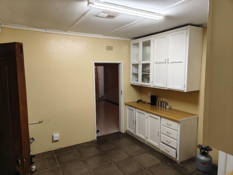 A functional scullery or utility area featuring built-in white cabinetry, laminate countertops, and tiled flooring, offering potential for modernization and improved storage utility.