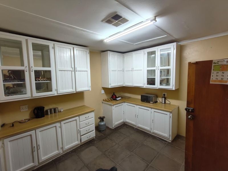 A functional kitchen featuring white cabinetry, laminate countertops, and tiled flooring, offering a practical layout with ample storage space.