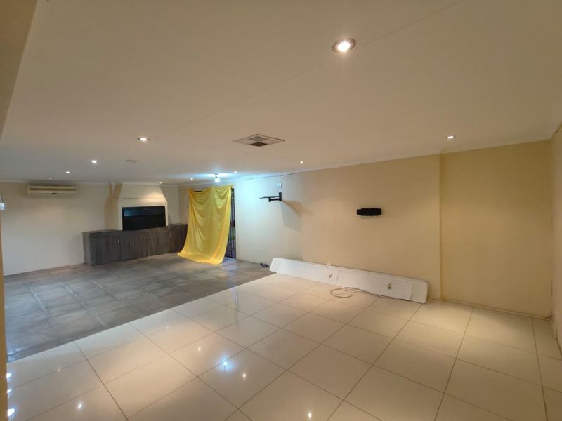 Spacious open-plan living area featuring tiled flooring, recessed lighting, a built-in fireplace, and a wall-mounted air conditioning unit.