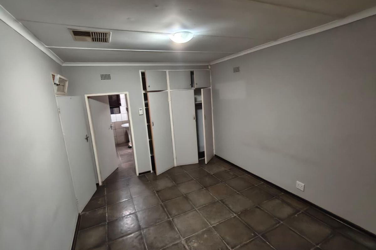 An empty bedroom featuring built-in cupboards, tiled flooring, and a ceiling vent, providing a blank canvas for renovation or restyling.