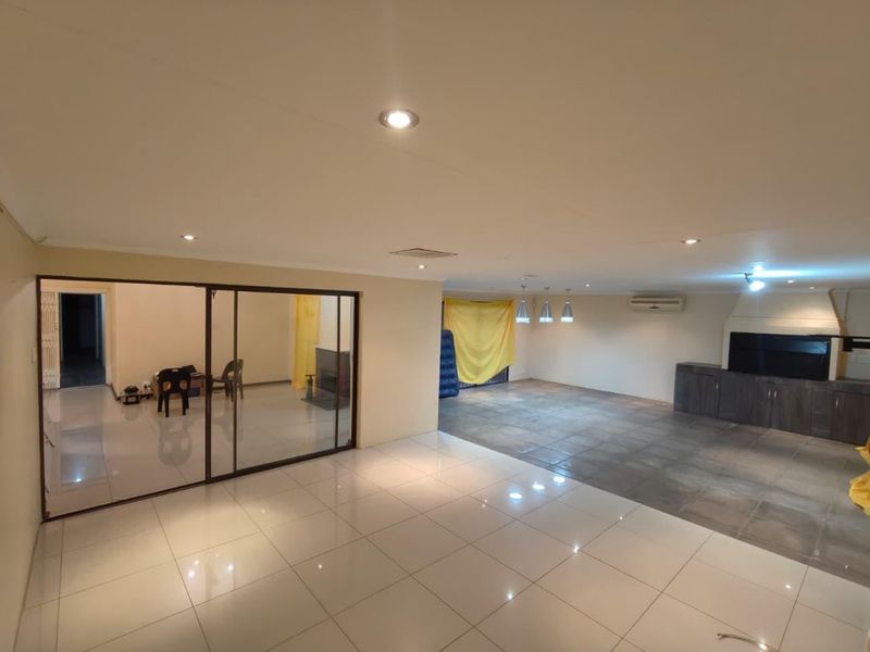 Spacious open-plan living area featuring tiled floors, recessed lighting, a built-in braai, and sliding glass doors leading to an adjacent room.
