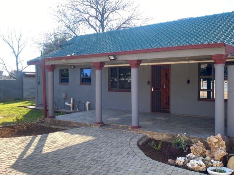 A well-maintained rear exterior featuring a covered patio with decorative columns, a tiled roof, and a paved driveway leading to the entrance.