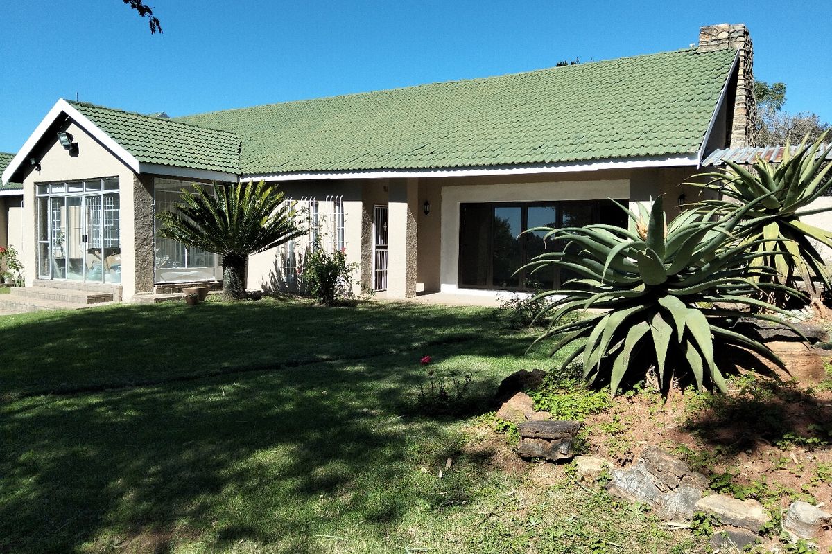 Rear view of a single-story house featuring a green tiled roof, large sliding glass doors, and a spacious garden with established landscaping.