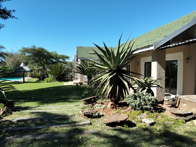 A spacious rear garden featuring a well-maintained lawn, mature landscaping, and a view of the swimming pool area adjacent to the house.