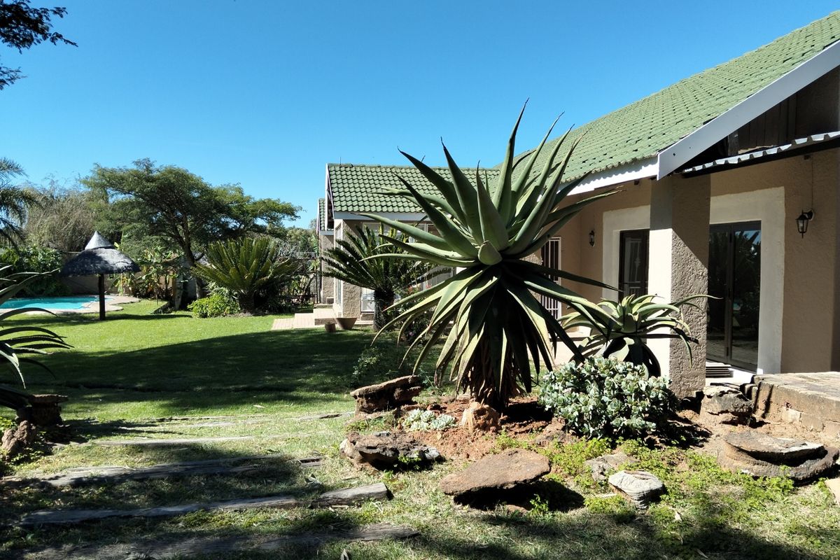 A spacious rear garden featuring a well-maintained lawn, mature landscaping, and a view of the swimming pool area adjacent to the house.