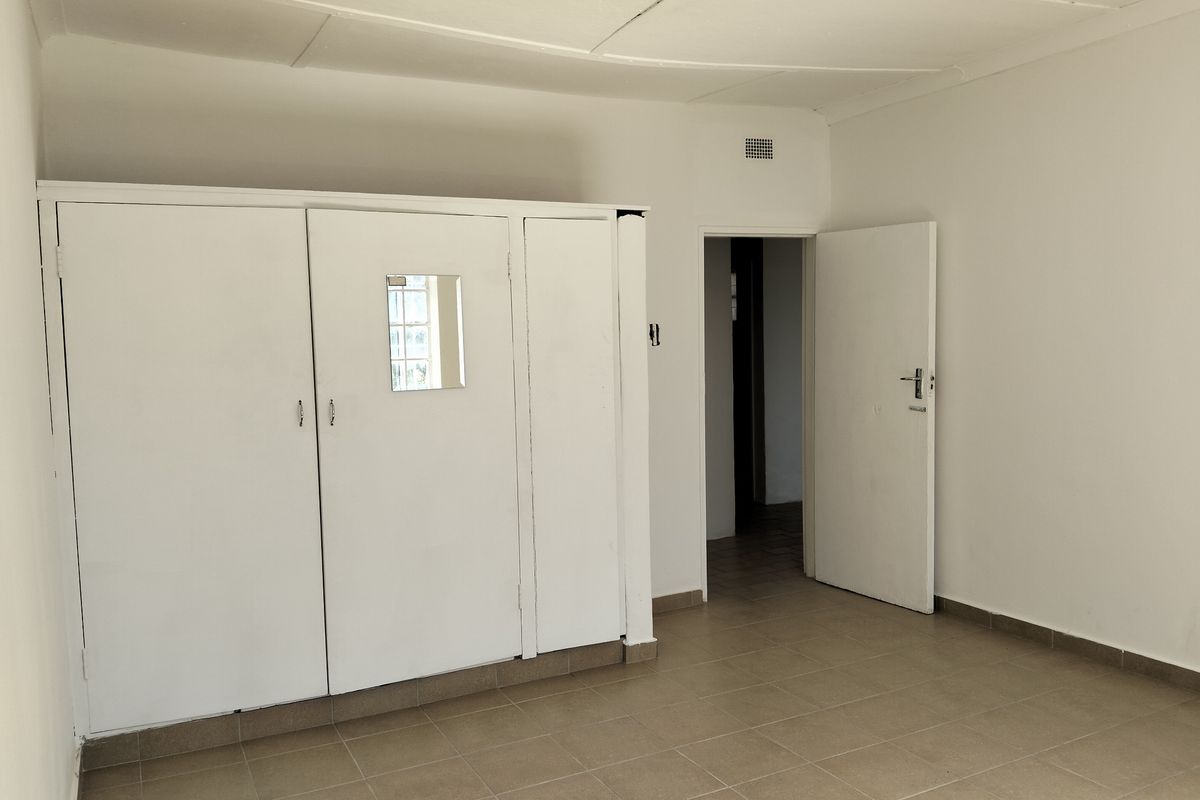 A simple bedroom featuring built-in white cupboards, tiled flooring, and a standard doorway leading to an adjacent space.
