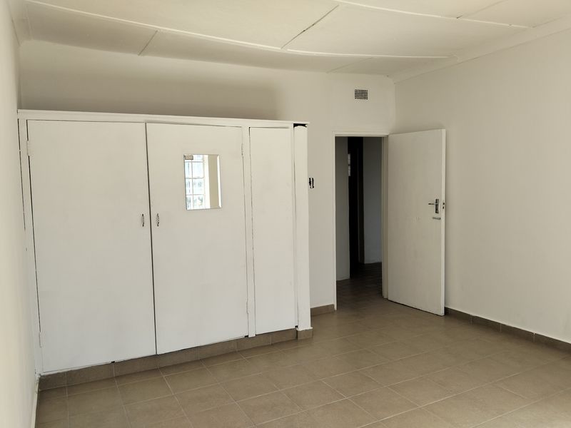 A simple bedroom featuring built-in white cupboards, tiled flooring, and a standard doorway leading to an adjacent space.
