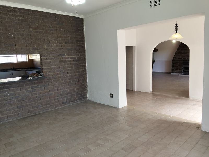 Open plan living area featuring a rustic face-brick feature wall, tiled flooring, and an arched entryway leading to an adjacent room.