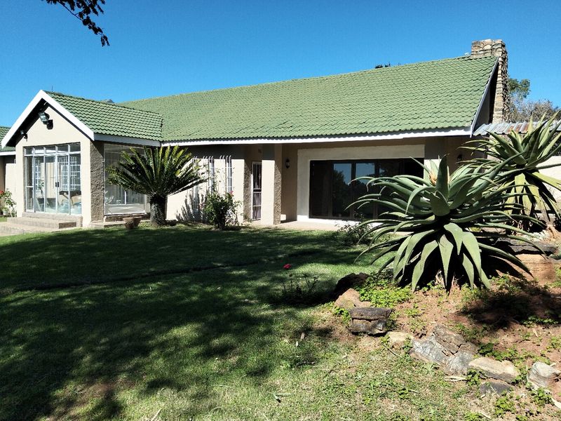 Rear view of a single-story house featuring a green tiled roof, large sliding glass doors, and a spacious garden with established landscaping.