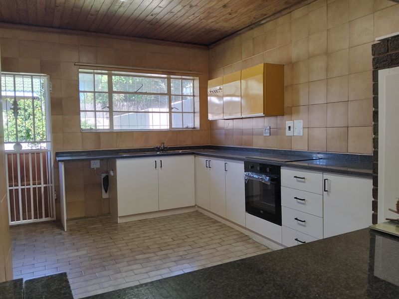 A functional kitchen featuring white cabinetry, dark countertops, a built-in oven, and a timber-paneled ceiling with tiled walls and flooring.