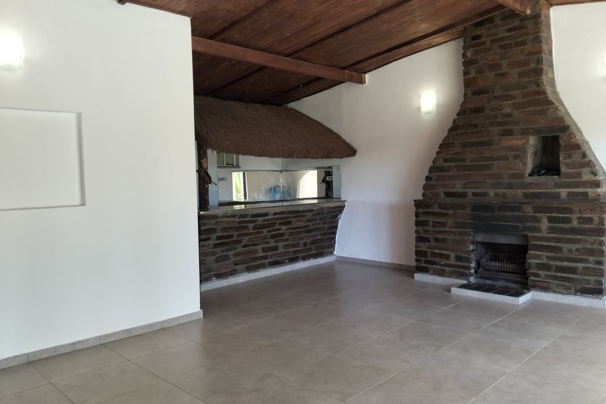 Spacious living area featuring a rustic brick fireplace, tiled flooring, and a built-in bar with a thatched roof detail.