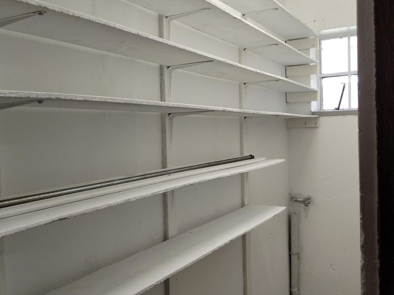 A functional utility or storage room featuring extensive built-in shelving, a small window for ventilation, and tiled flooring.