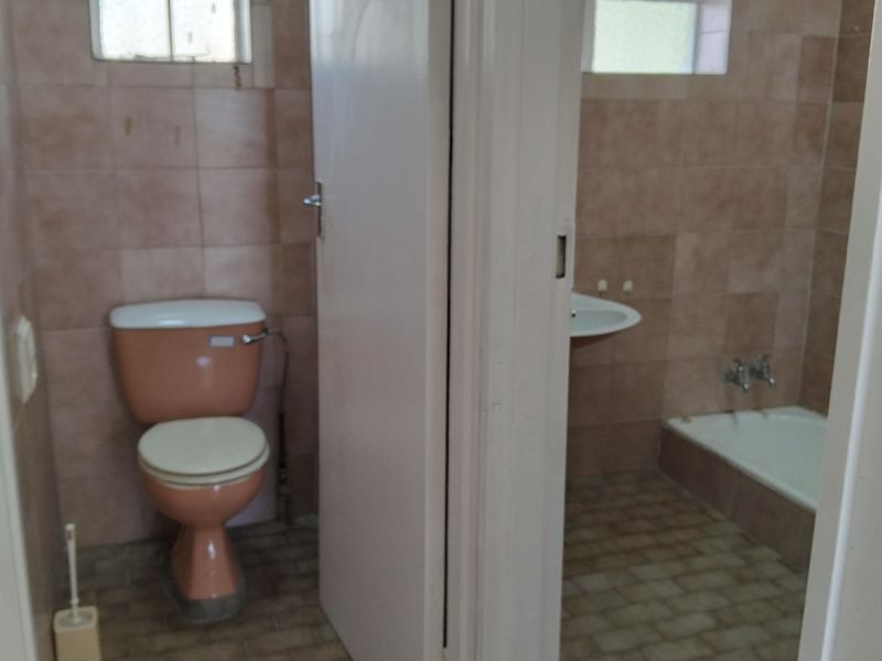 A dated bathroom featuring a separate toilet and a combined bath and basin area with original ceramic wall tiles and floor finishes.