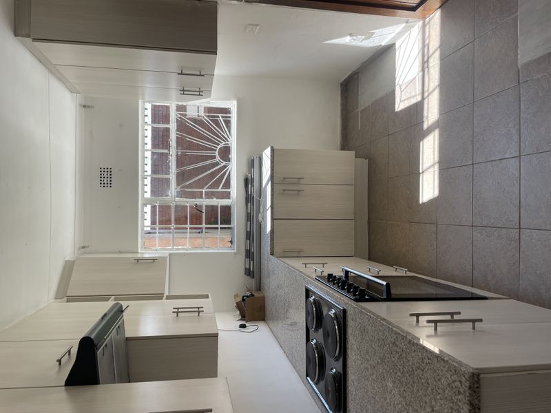 A clean, functional kitchen featuring light wood-finish cabinetry, granite countertops, a built-in electric hob and oven, and tiled flooring.
