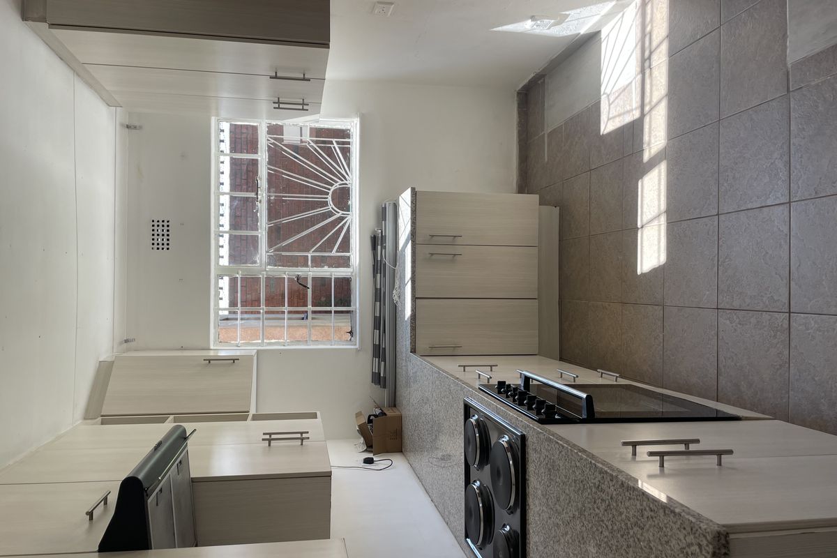 A clean, functional kitchen featuring light wood-finish cabinetry, granite countertops, a built-in electric hob and oven, and tiled flooring.