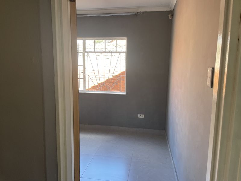 An empty bedroom featuring tiled flooring, grey painted walls, and a window fitted with security bars.