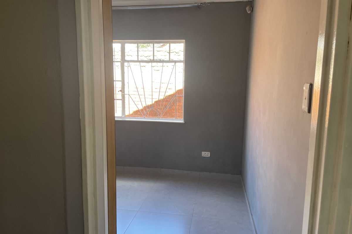 An empty bedroom featuring tiled flooring, grey painted walls, and a window fitted with security bars.