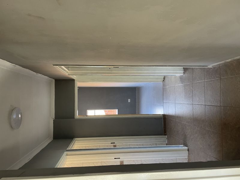 A vacant hallway featuring tiled flooring and unfinished wall surfaces, providing access to multiple rooms within the property.