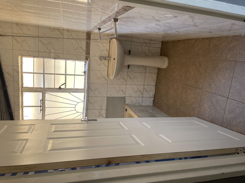 A compact bathroom featuring a pedestal basin, built-in bathtub, and tiled finishes. The space requires minor repairs to wall tiling and general cosmetic updates.