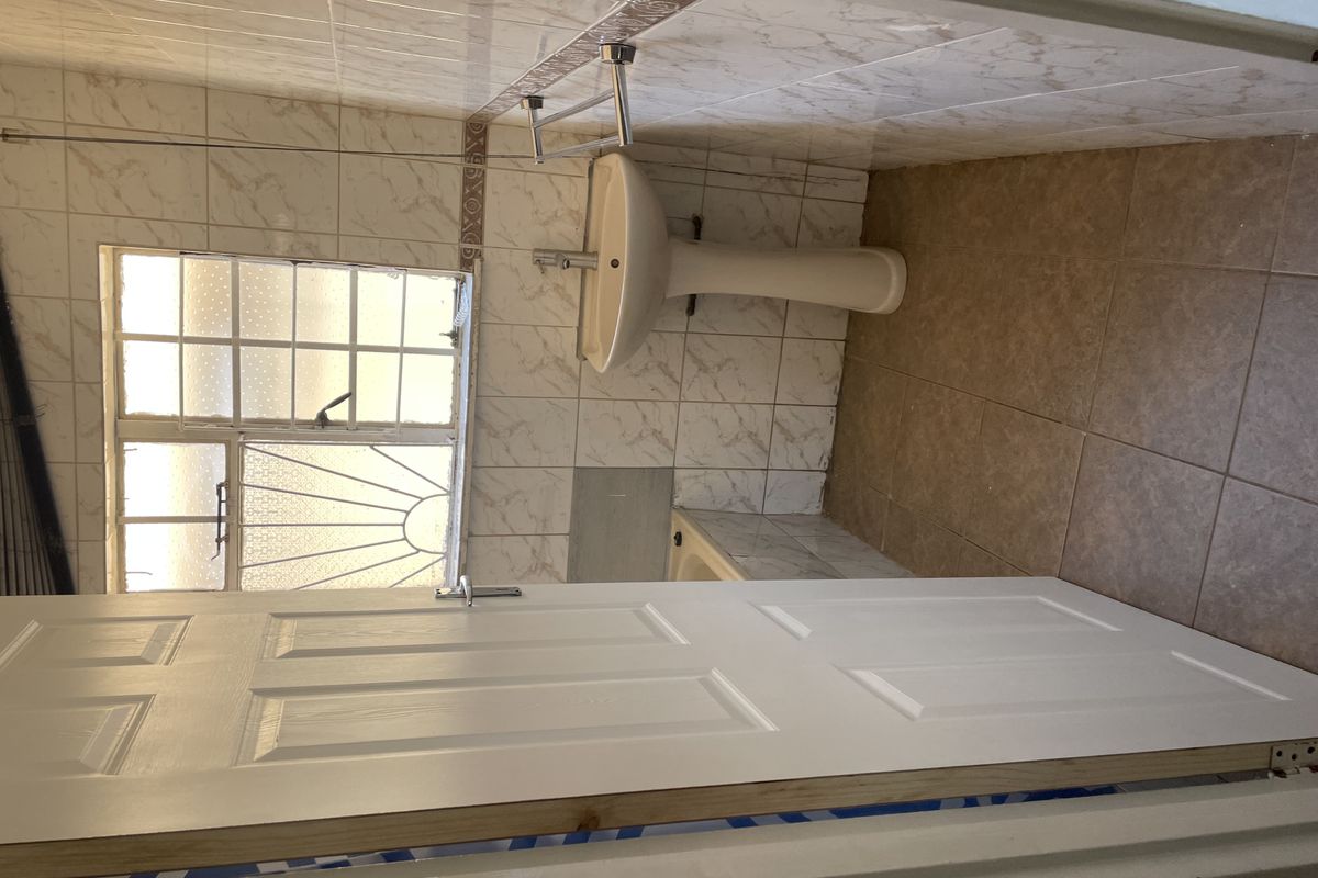 A compact bathroom featuring a pedestal basin, built-in bathtub, and tiled finishes. The space requires minor repairs to wall tiling and general cosmetic updates.
