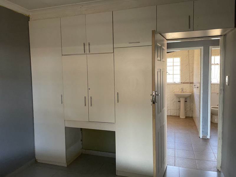 A bedroom featuring built-in cupboards with an integrated desk space, leading into an en-suite bathroom with tiled finishes.