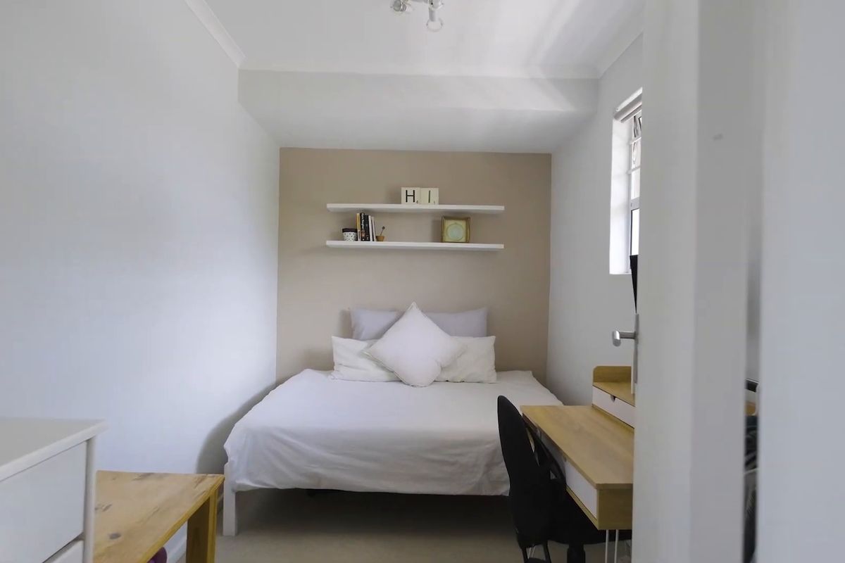 A compact bedroom featuring neutral wall tones, built-in shelving, and a window providing natural light.