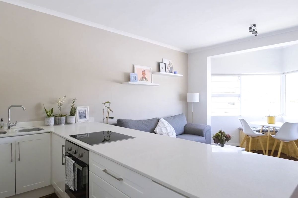 An open-plan living area featuring a modern kitchen with white cabinetry, stone countertops, a built-in hob and oven, and a bright dining nook.