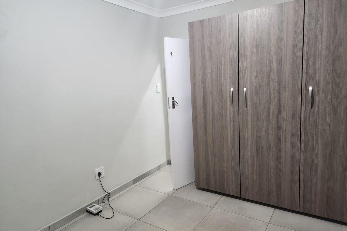 A clean, empty bedroom featuring modern wood-grain built-in cupboards, neutral tiled flooring, and a crisp white finish.
