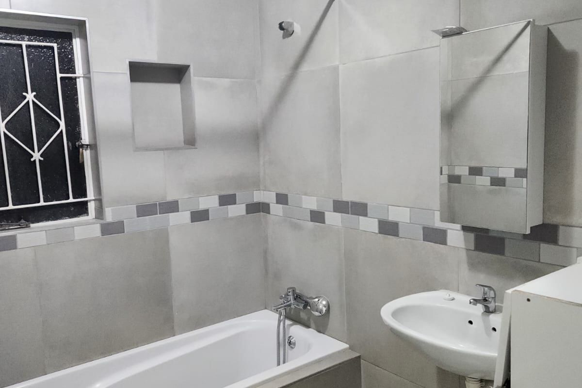 A modern, neutral-toned bathroom featuring a bathtub, wall-mounted basin, built-in wall niche, and tiled finishes throughout.