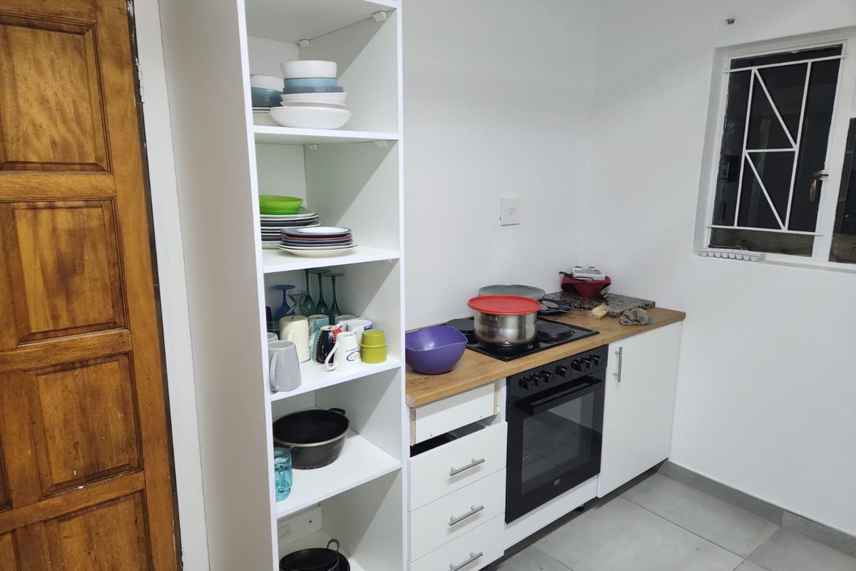 Compact kitchen featuring a built-in oven, hob, and white cabinetry with open shelving, finished with tiled flooring.
