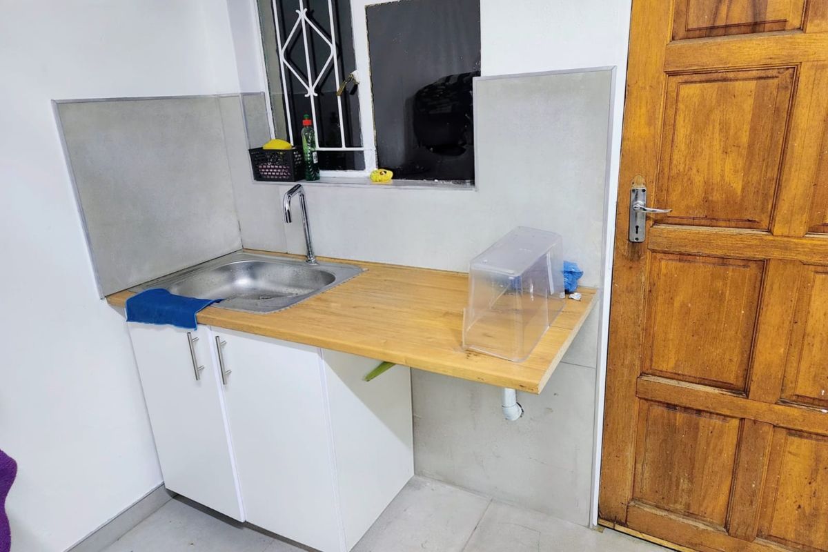 A functional scullery area featuring a stainless steel sink, wooden countertop, and white base cabinetry, adjacent to a timber door.