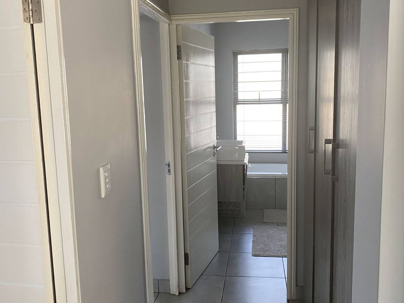 A clean, neutral hallway featuring tiled flooring and built-in cupboards, providing access to an adjacent bathroom.