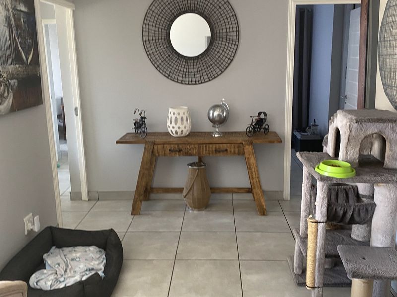 A well-maintained hallway featuring neutral grey walls, recessed downlighting, and large format floor tiles, providing access to adjacent rooms.
