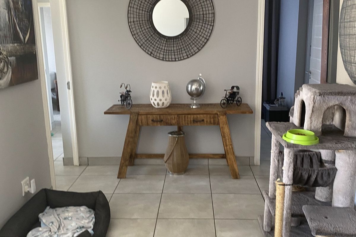 A well-maintained hallway featuring neutral grey walls, recessed downlighting, and large format floor tiles, providing access to adjacent rooms.
